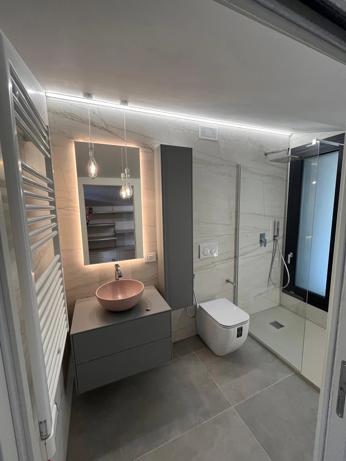 Il bagno con rivestimenti chiari, lavabo rosa e doccia in vetro