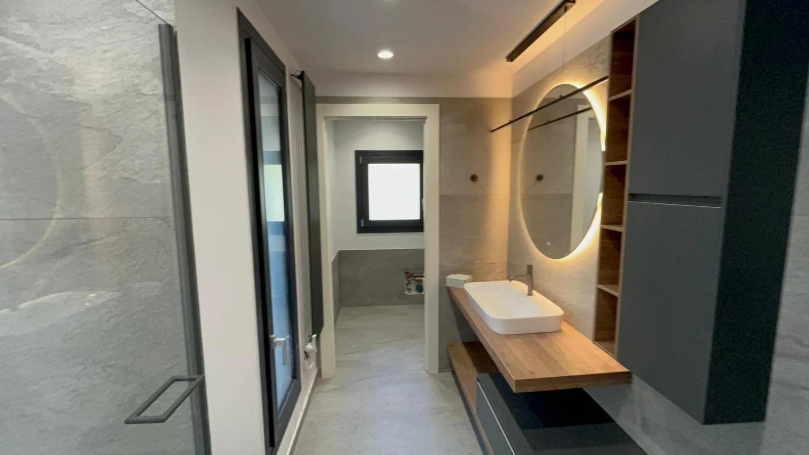 Il bagno con piano in legno e specchio tondo illuminato